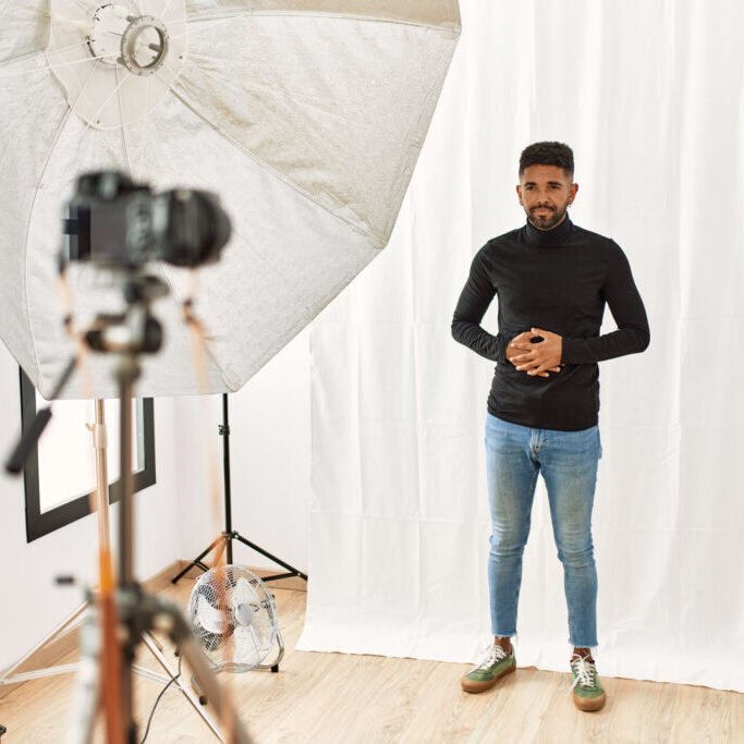 Young hispanic man with beard posing as model at photography studio with hand on stomach because indigestion, painful illness feeling unwell. ache concept.