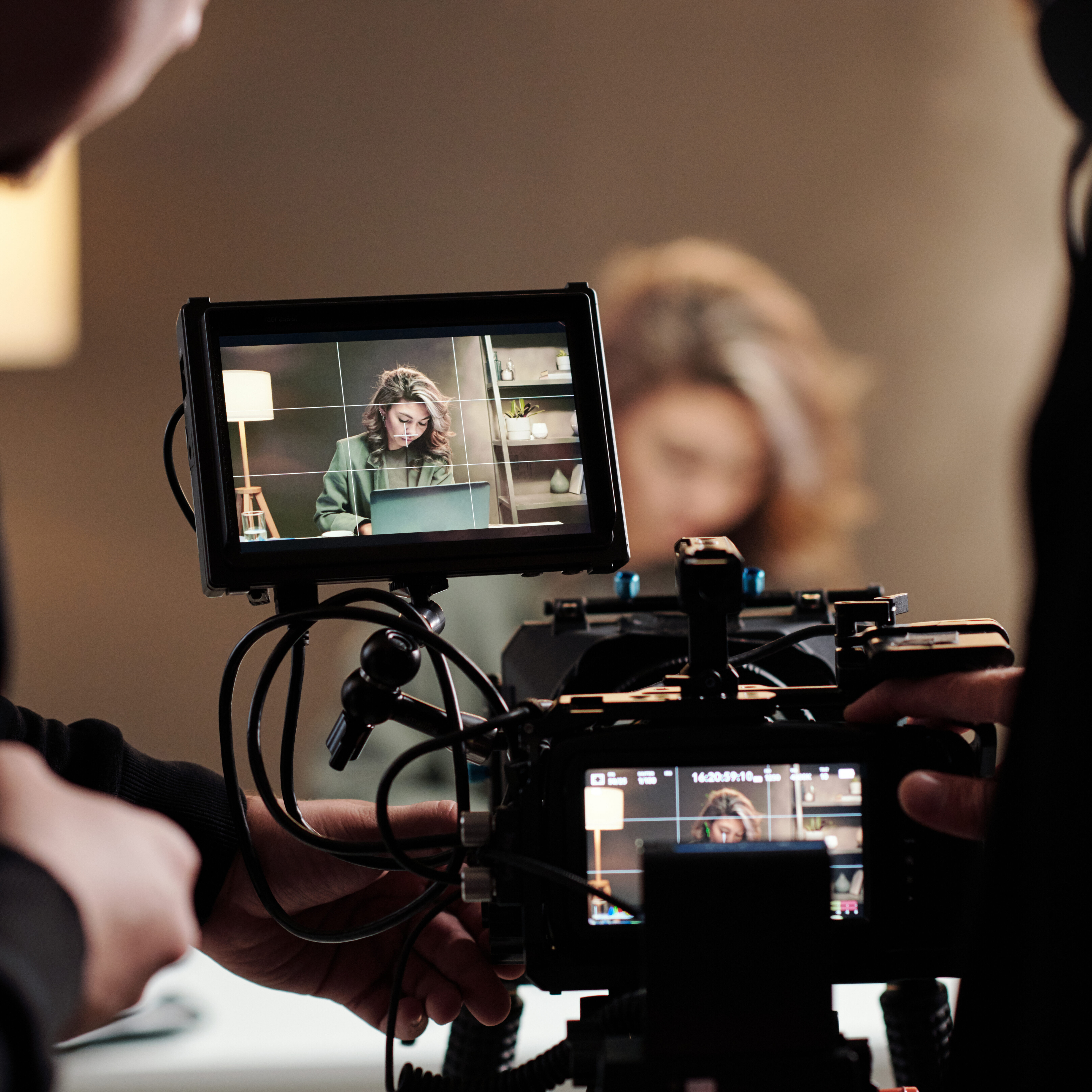 Close-up of steadicam screens with female model using laptop by table during commercial being shot by cameraman and his assistant