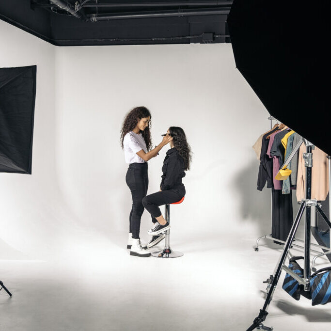 Stock photo of young woman applying make up to her client in studio over white background.